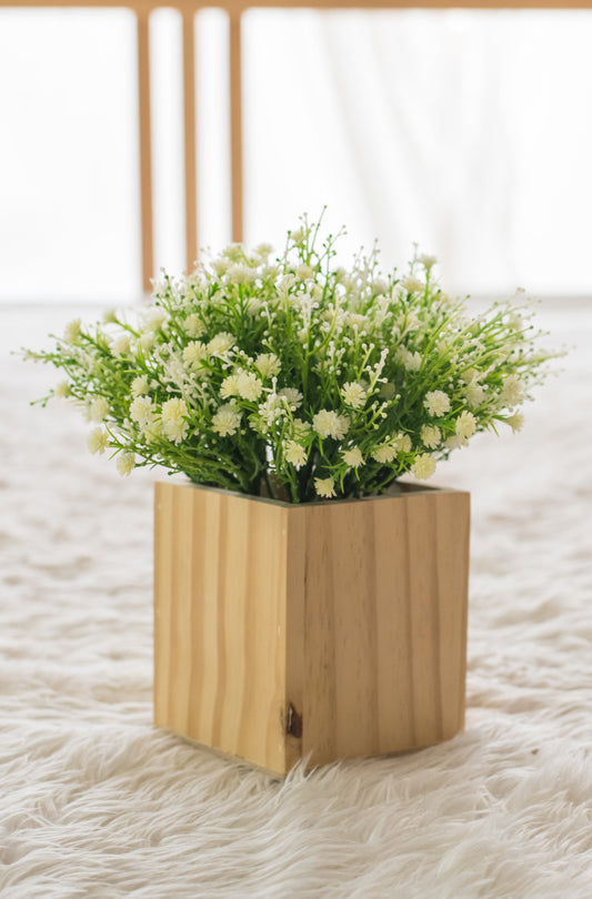 Minimalist wooden planter box with white faux flowers placed on a soft textured surface – modern home décor accent.