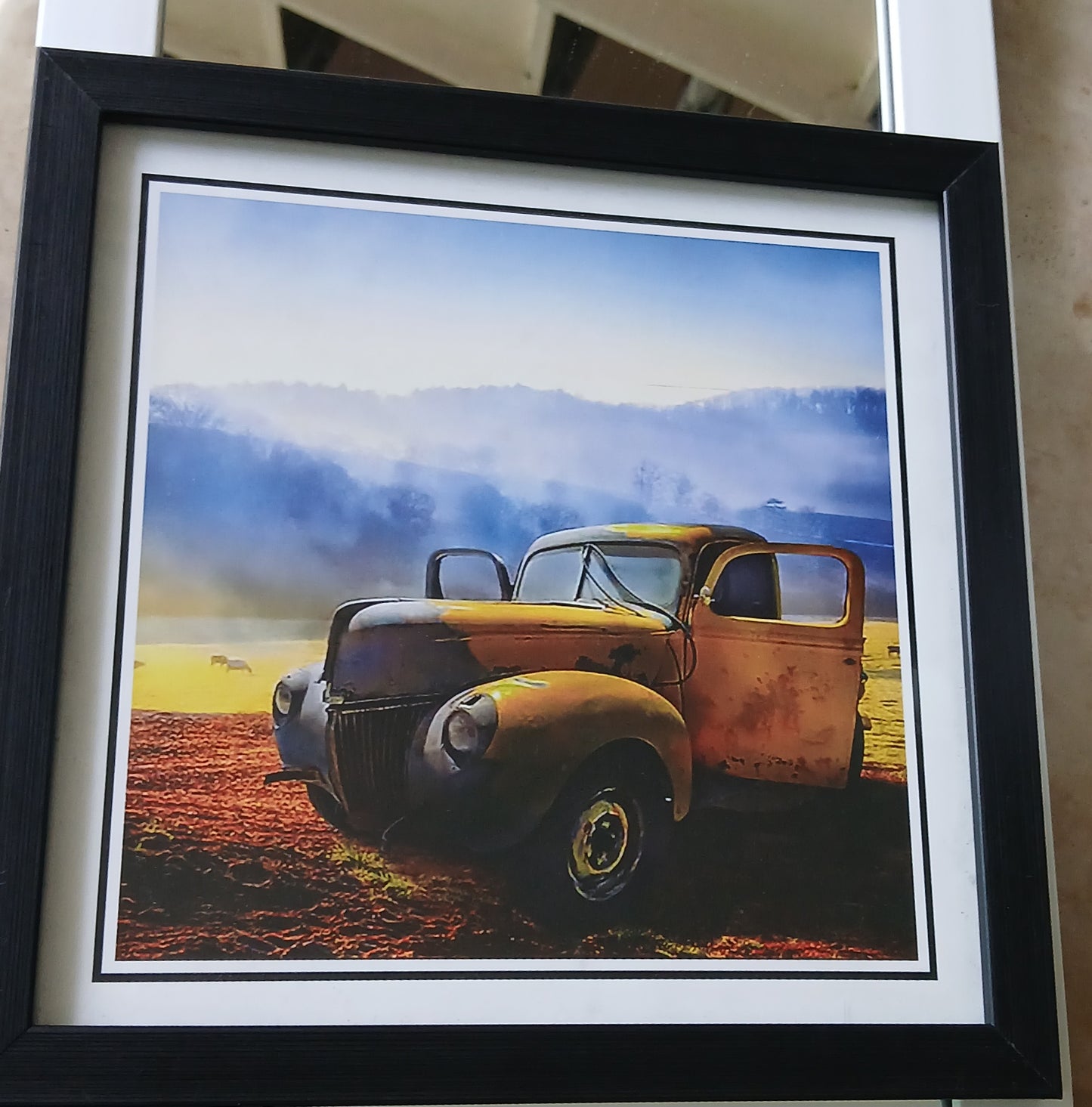 Framed picture of an old yellow truck on a field with a blue sky.