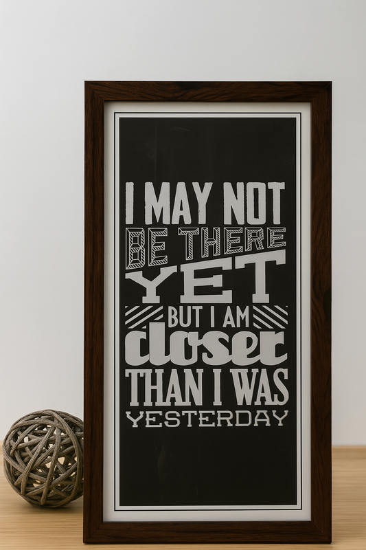 Framed inspirational wall art with quote: “I may not be there yet, but I am closer than yesterday” in black and white wooden frame.